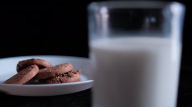 Bir bardak sütün arkasındaki tabakta el yapımı kurabiyeler.