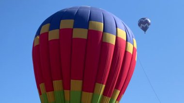 Mavi gökyüzünün altında renkli bir sıcak hava balonunu ısıtıp şişiriyor.