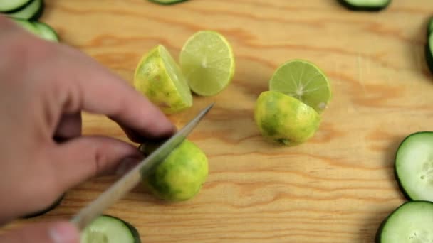Ręce krojące limonki na drewnianej desce do krojenia z plastrami ogórka — Wideo stockowe