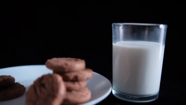 Gestapelte Kekse auf weißem Teller und Glas Milch mit schwarzem Hintergrund — Stockvideo