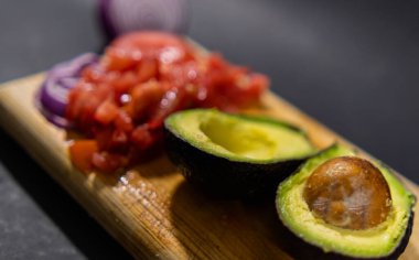 Doğranmış domates, dilimlenmiş soğan ve kesme tahtasında yarım avokado.