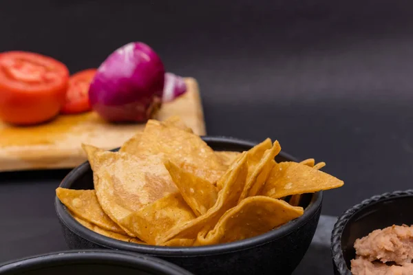 Tortilla chipsy i fasola obok krojone warzywa z czarnym tle — Zdjęcie stockowe