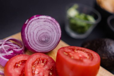 Kesme tahtasında dilimlenmiş domates ve soğan, siyah ve bulanık arka planda.