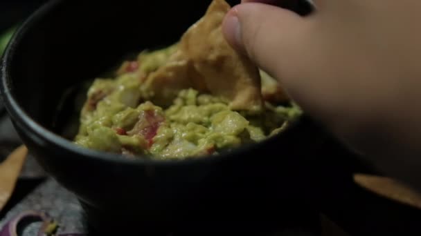 Hand dipping tortilla chip in bowl of guacamole surrounded by tortilla chips — Stock Video