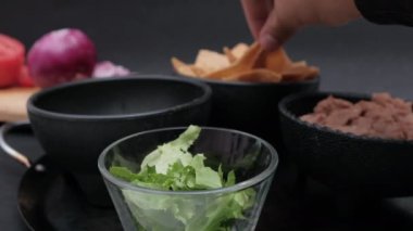 Bir kase tortilla cipsi, yeniden kızartılmış fasulye ve siyah arkaplanlı marul.