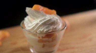 Tahta yüzeyde bir fincan şeftali, krema ve meyve dilimleri.