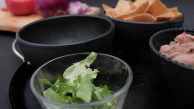 Dilimlenmiş sebze, bir kase tortilla cipsi ve siyah arkaplanlı fasulye.