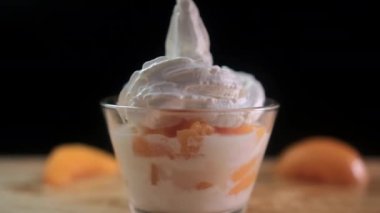 Tahta yüzeyde bir fincan şeftali, krema ve meyve dilimleri.