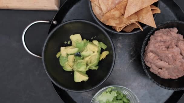 Krájená zelenina a misky tortilla chipsů a avokáda na černém povrchu — Stock video