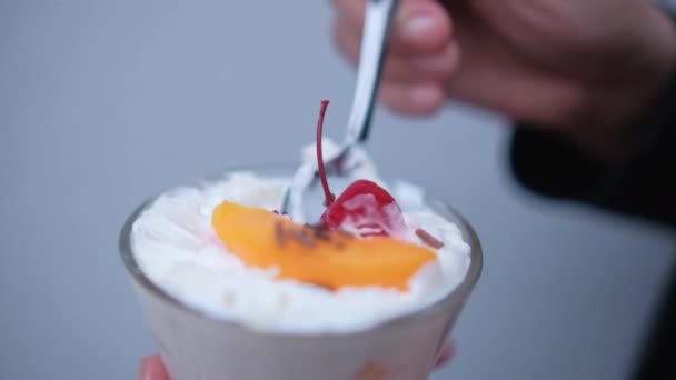 Mani che tengono cucchiaio e tazza di pesche e crema con sfondo azzurro — Video Stock