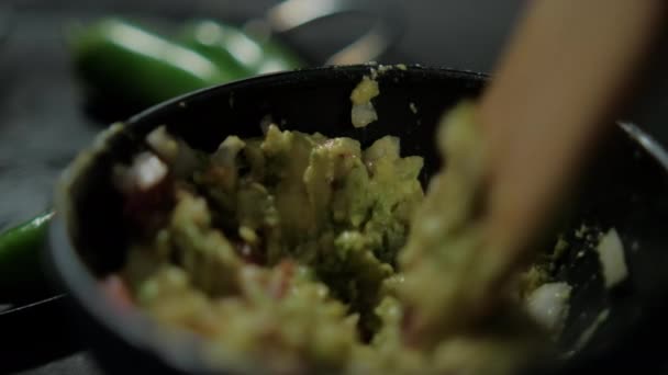 Cuillère en bois préparant guacamole avec des piments flous comme fond — Video