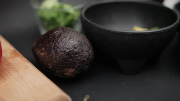 Πιπεριές τσίλι και μπολ με ψιλοκομμένο αβοκάντο και φασόλια σε μαύρη επιφάνεια — Αρχείο Βίντεο