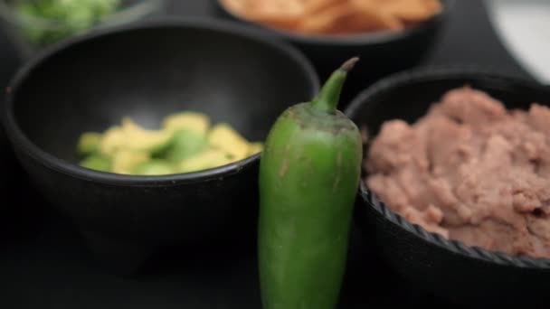 Pimentos e tigelas de abacate picado e feijão frito na superfície preta — Vídeo de Stock
