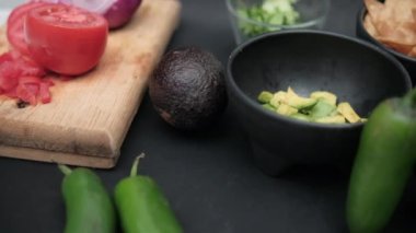 Siyah yüzeyde acı biber ve bir kase doğranmış avokado ve tortilla cipsi.