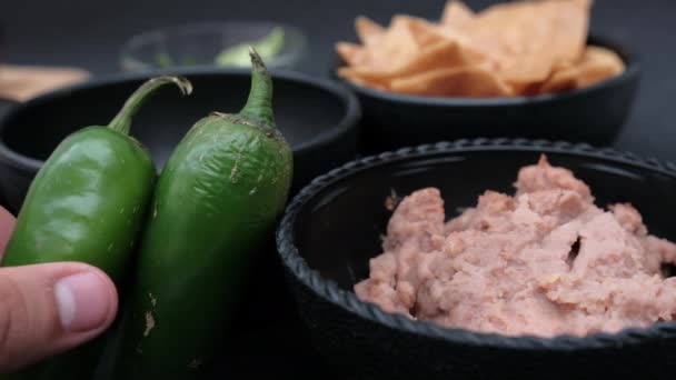 Chili peppers leaning against bowls of tortilla chips and refried beans — Stock Video