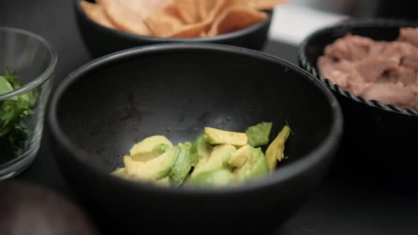 Cuencos de aguacate picado, chips de tortilla y frijoles refritos en la superficie negra — Vídeos de Stock