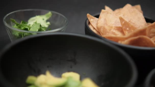 Tigelas de abacate picado, batatas fritas de tortilla e feijão refrito na superfície preta — Vídeo de Stock