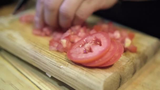 Dłonie ostrożnie kroją kawałki pomidorów nad drewnianą deską do krojenia — Wideo stockowe