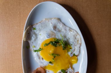 Lezzetli sahanda yumurta ve pastırma şeritleri ve beyaz tabakta doğranmış otlar.