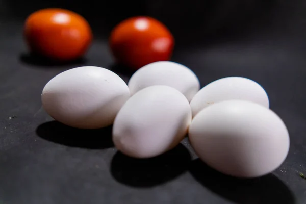 Five fresh white eggs and tomatoes on black surface — Stock Photo, Image