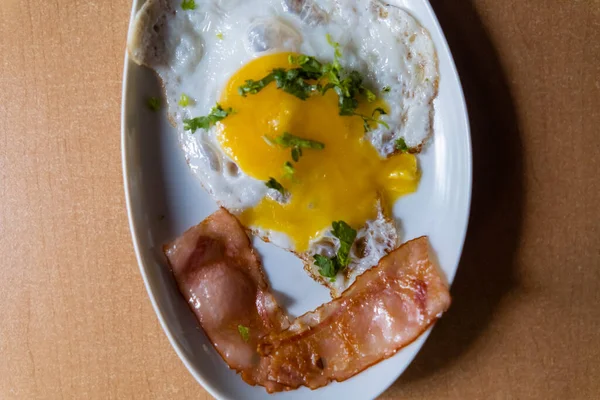 Läckra stekta ägg och bacon ränder med hackade örter på vit platta — Stockfoto