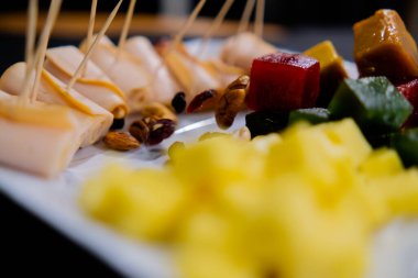 Jambonlu börek, meyve ezmesi, peynir küpleri ve bulanık arkaplanlı fındıklar.