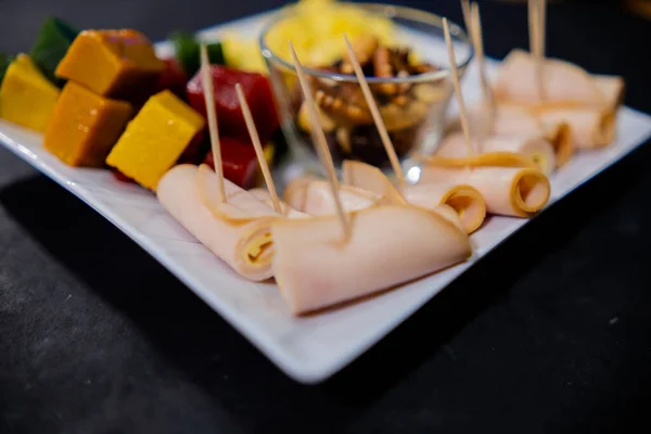 Šunkové závitky, nakrájená ovocná pasta, kostky sýra a ořechy na čtvercový bílý talíř — Stock fotografie