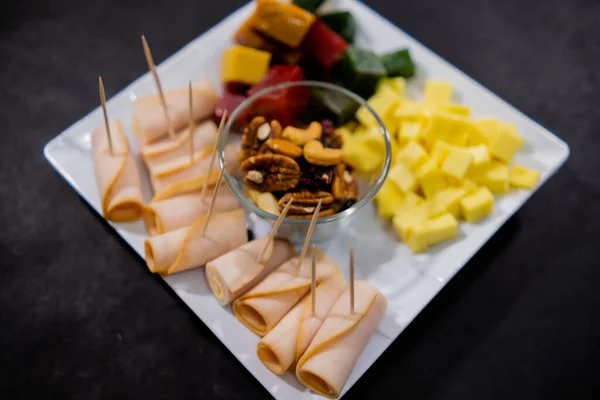 Šunkové závitky, nakrájená ovocná pasta, kostky sýra a ořechy na čtvercový bílý talíř — Stock fotografie