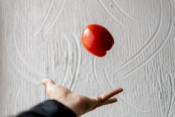 Hand throwing tomato with white textured wall as background