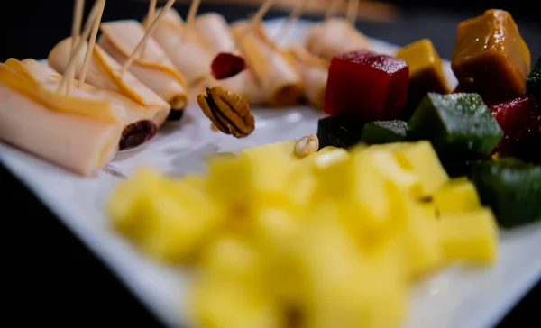 Šunkové závitky, ovocná pasta, kostky sýra a ořechy na bílém talíři — Stock fotografie