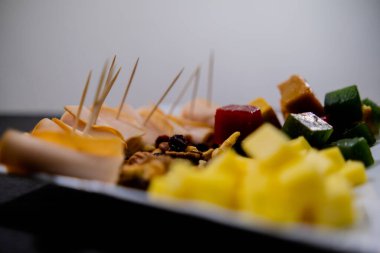 Bir tabak jambon, meyve ezmesi, peynir küpleri ve beyaz arka planda fındık.