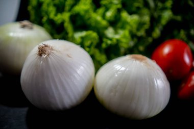 Domates, soğan ve siyah arkaplanın üzerinde büyük marul.