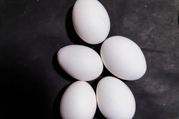 Five fresh white eggs lying down on black surface — Stock Photo, Image