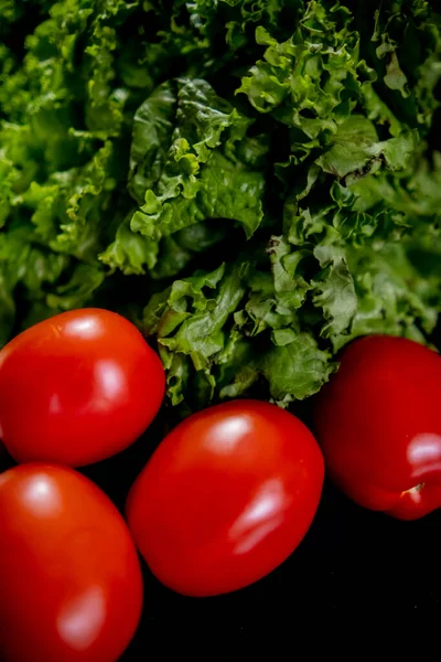 Tomaten en grote Batavia sla boven zwarte achtergrond — Stockfoto