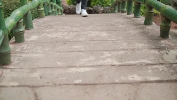 Ben i svarta byxor och vita sneakers går på gamla bron — Stockvideo