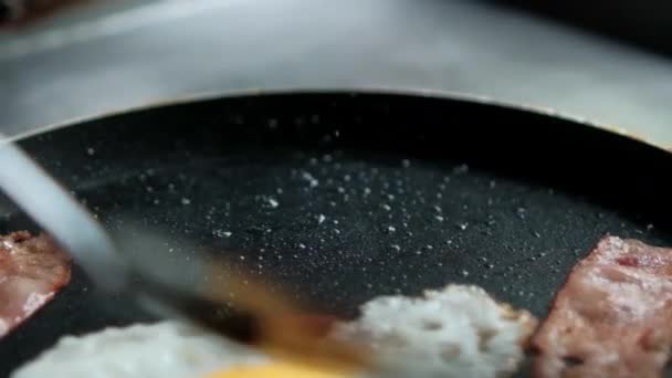 Espátula levantando la tira de tocino de la sartén con aceite y huevo frito — Vídeo de stock
