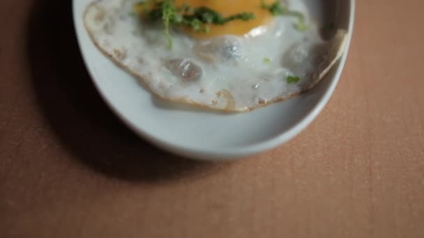 Delicious fried egg and bacon stripes with chopped herbs on white plate — Stock Video