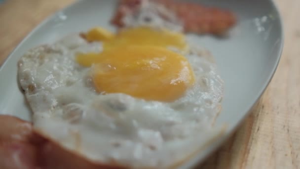 Вкусные жареные яйца и полоски бекона на белой тарелке — стоковое видео