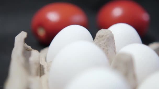 Zes witte eieren in karton en twee tomaten op zwarte ondergrond — Stockvideo