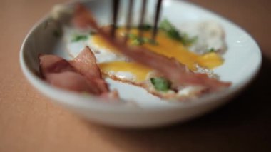 Çatal, lezzetli pastırma şeritlerini kızarmış yumurta ve doğranmış otlarla tabağa koyuyor.