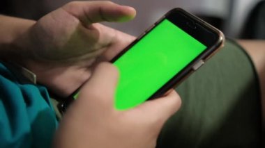 Parlak yeşil ekranlı siyah bir akıllı telefon tutan eller.