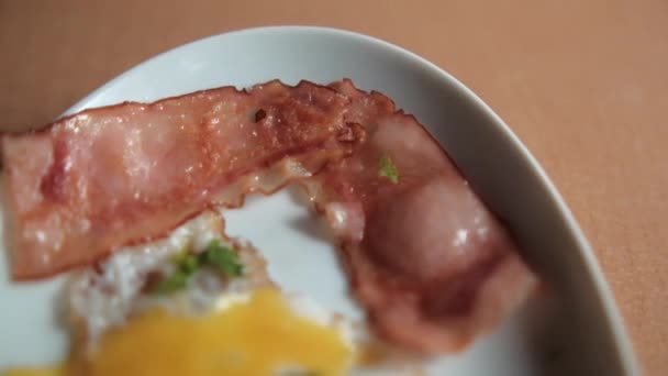 Finom sült tojás és szalonna csíkok apróra vágott gyógynövényekkel fehér tányéron — Stock videók