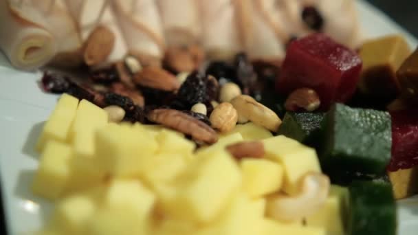 Šunkové závitky, ovocná pasta, kostky sýra, ořechy, suché brusinky na bílém talíři — Stock video