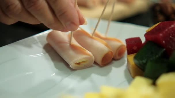 Manos colocando rollos de jamón en un plato con pasta de frutas cortadas en cubitos y cubos de queso — Vídeo de stock