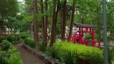 Arka planda geleneksel Japon kapısı ve göleti olan parkta toprak yollar.