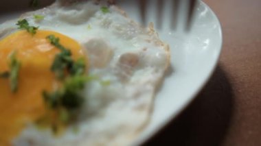 Pastırma şeritleri ve doğranmış otlarla tabakta leziz kızarmış yumurta dürten çatal.