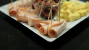 Jambonlu dürüm, doğranmış meyve ezmesi, beyaz tabakta peynir ve fındık.