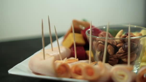 Šunkové závitky, nakrájená ovocná pasta, kostky sýra a ořechy na bílém talíři — Stock video