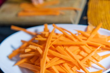 Beyaz tabakta ince havuç dilimleri ve bulanık arka plan.