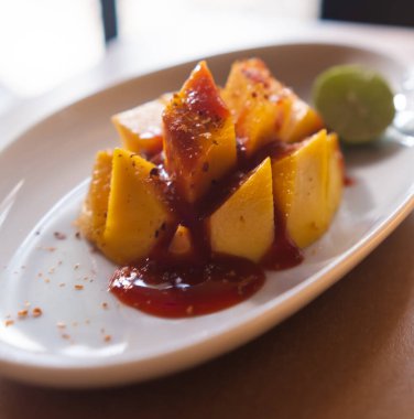 Plate of chopped mango with Mexican chamoy sauce and blurry background clipart